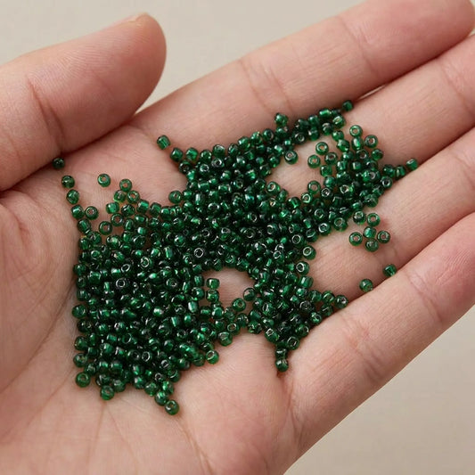 Emerald lined glass seed beads 2mm (12/0) displayed in hand for size reference with transparent emerald green glass and silver-lined finish