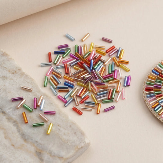 Mixed color 2x6mm long tube lined cylinder glass seed beads displayed with jewelry making materials