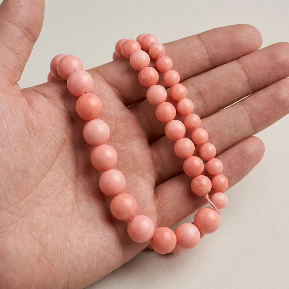 Pink coral round beads shown on hand for size and scale comparison
