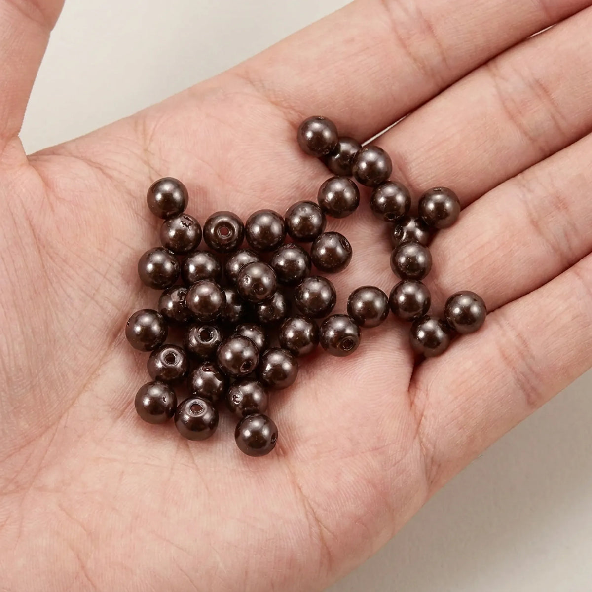 Chocolate glass pearl beads shown in hand for size reference