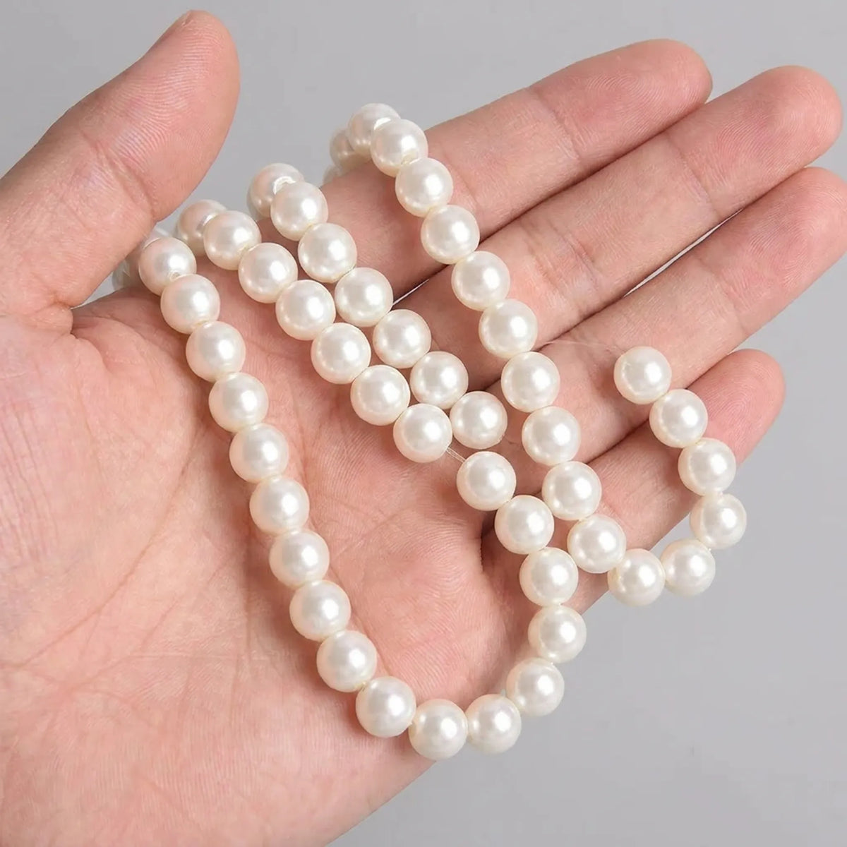 Cream glass pearl round beads shown in hand for size comparison