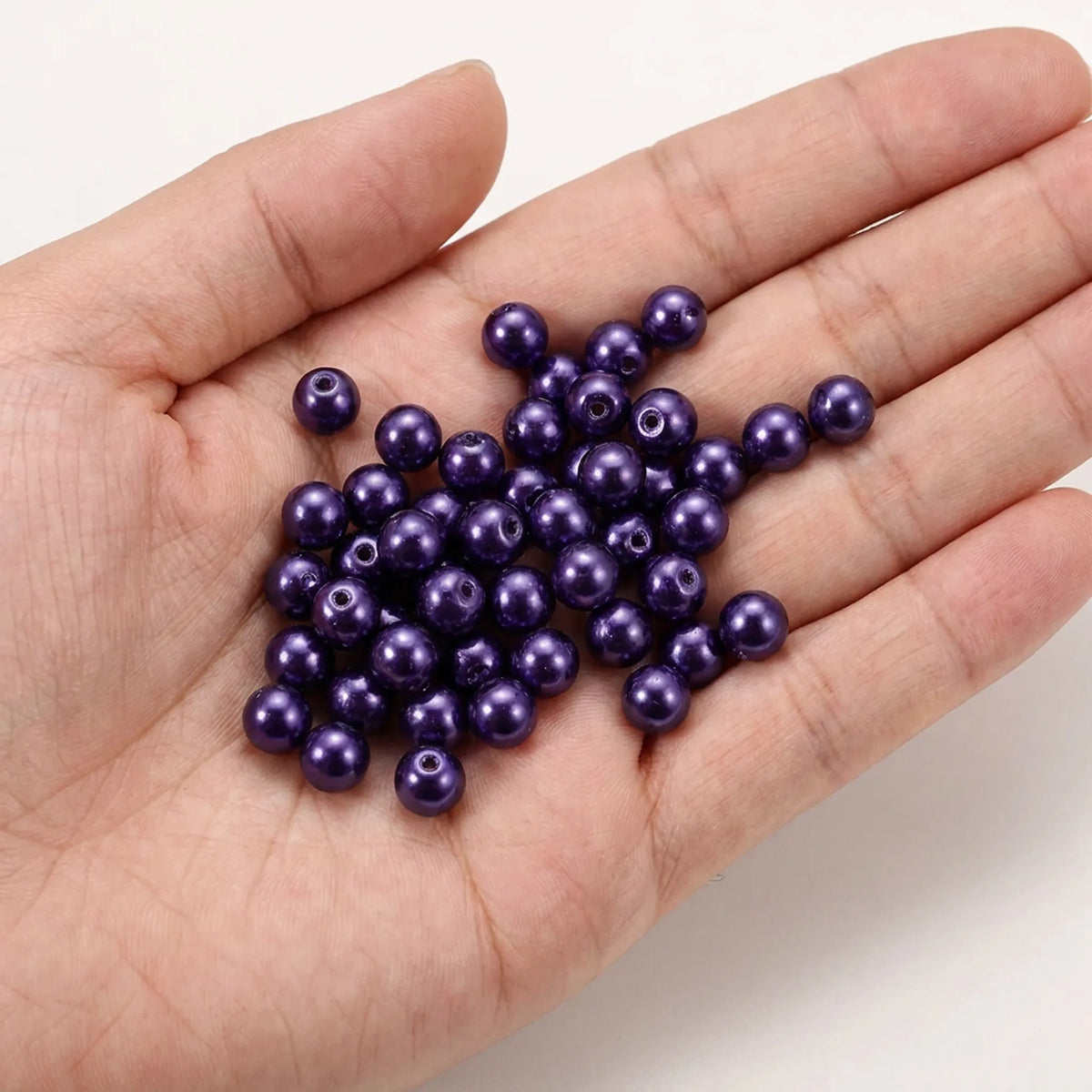 Dark purple glass pearl beads shown in hand for size reference