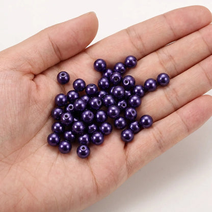 Dark purple glass pearl beads shown in hand for size reference
