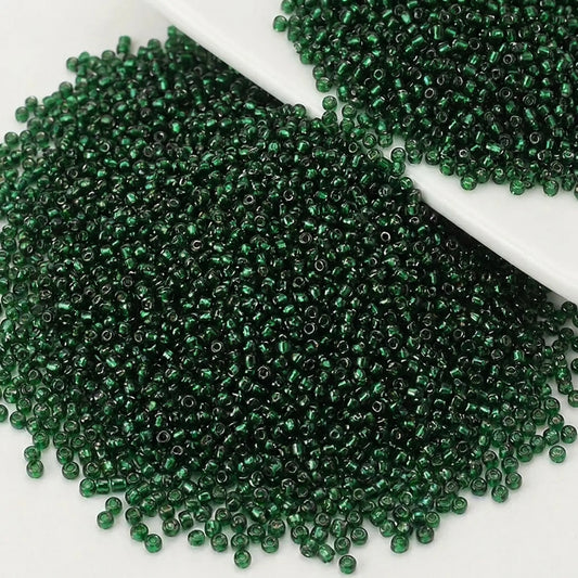 Emerald lined glass seed beads 2mm (12/0) for jewelry making scattered on a white surface showing their transparent green color and silver-lined centers