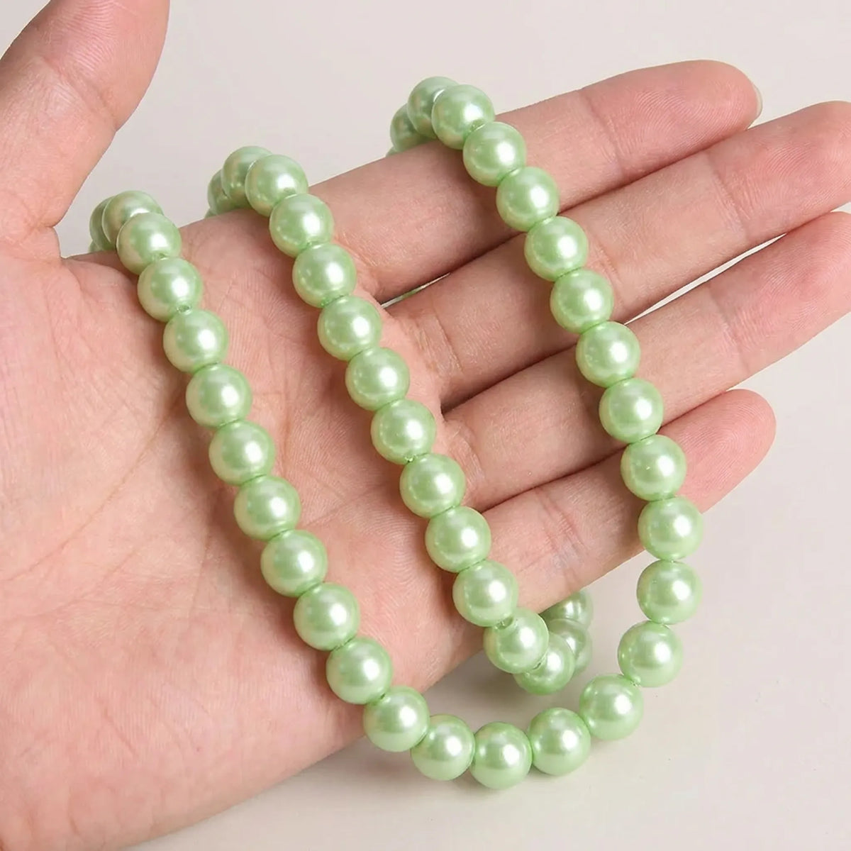 Green glass pearl round beads shown in hand for size comparison