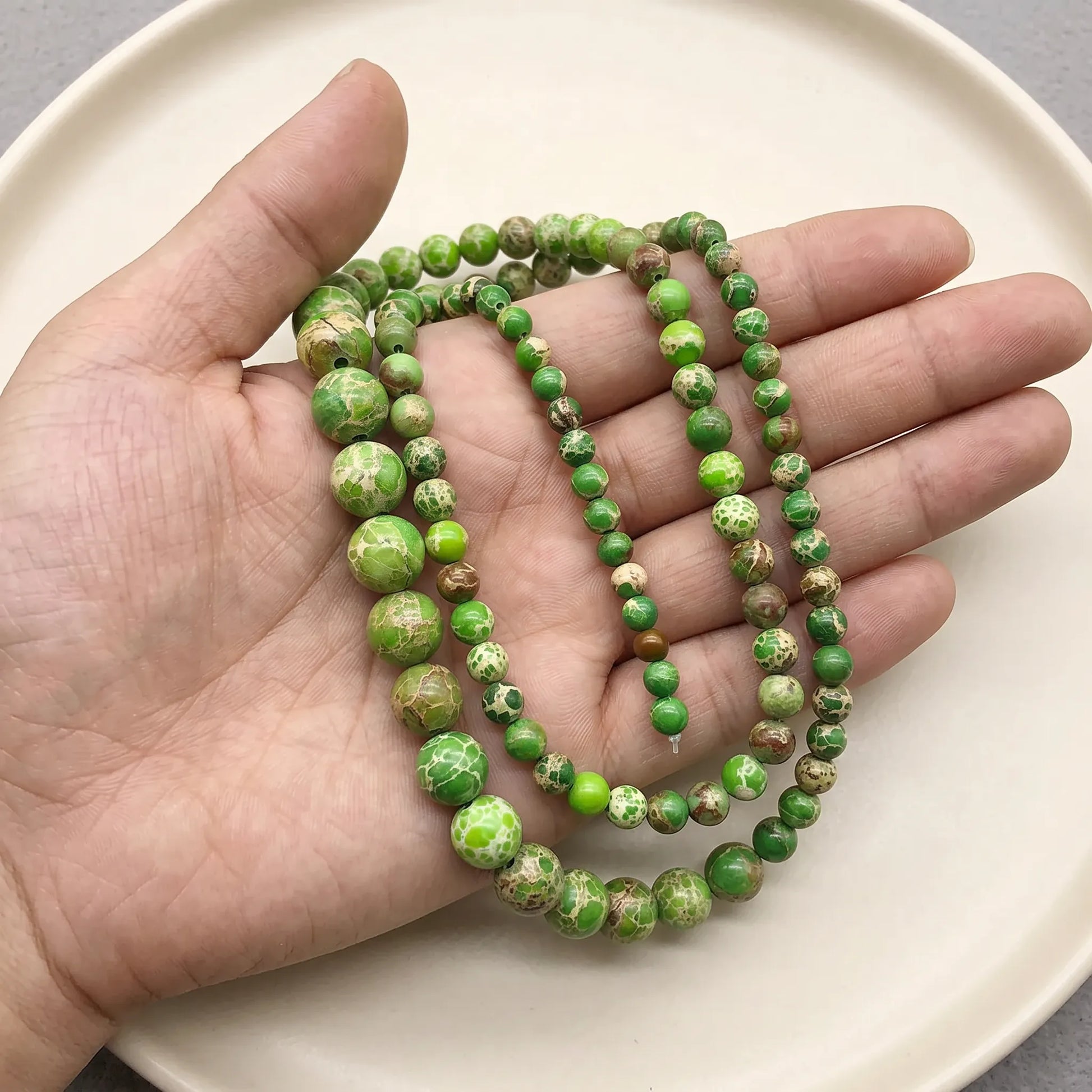 Green sea sediment jasper beads shown in hand for size comparison