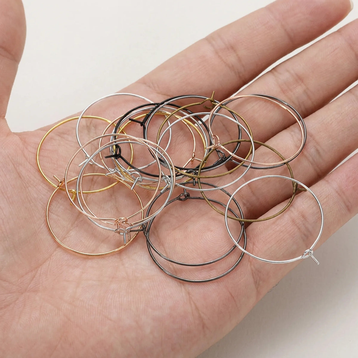 Mixed color large hoop earring wires for jewelry making shown in hand including gold silver bronze black rose gold and rhodium finishes