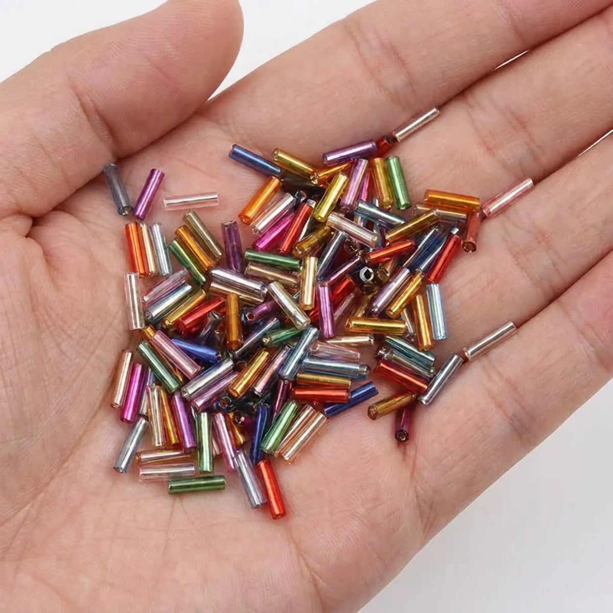 Mixed color 2x6mm long tube lined cylinder glass seed beads shown in hand for size reference