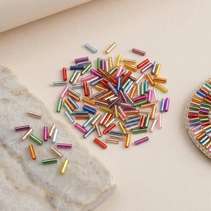 Mixed color 2x6mm long tube lined cylinder glass seed beads displayed with jewelry making materials