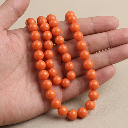 Orange coated opaque glass round beads shown in hand for size comparison