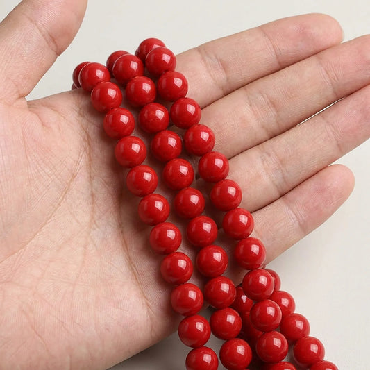 Red coated glass round beads shown in hand for size reference
