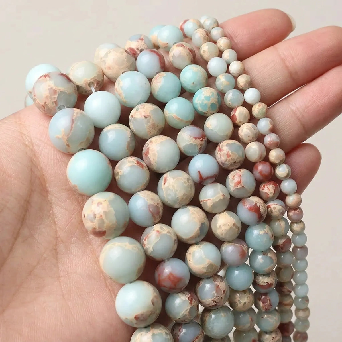 Natural Shoushan Jasper round beads in mixed 4–12mm sizes displayed in hand