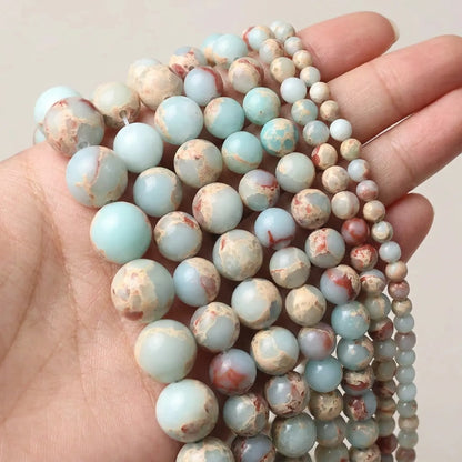 Natural Shoushan Jasper round beads in mixed 4–12mm sizes displayed in hand