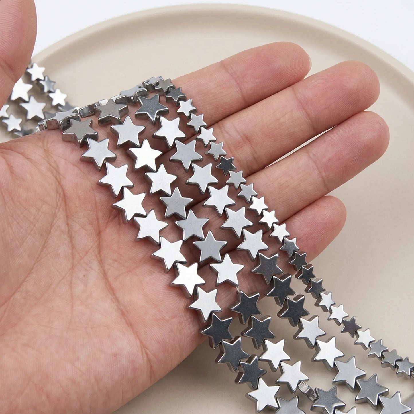 Silver flat star hematite beads shown in hand for size comparison