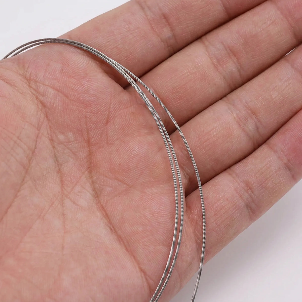 Stainless steel beading wire shown on hand for size reference