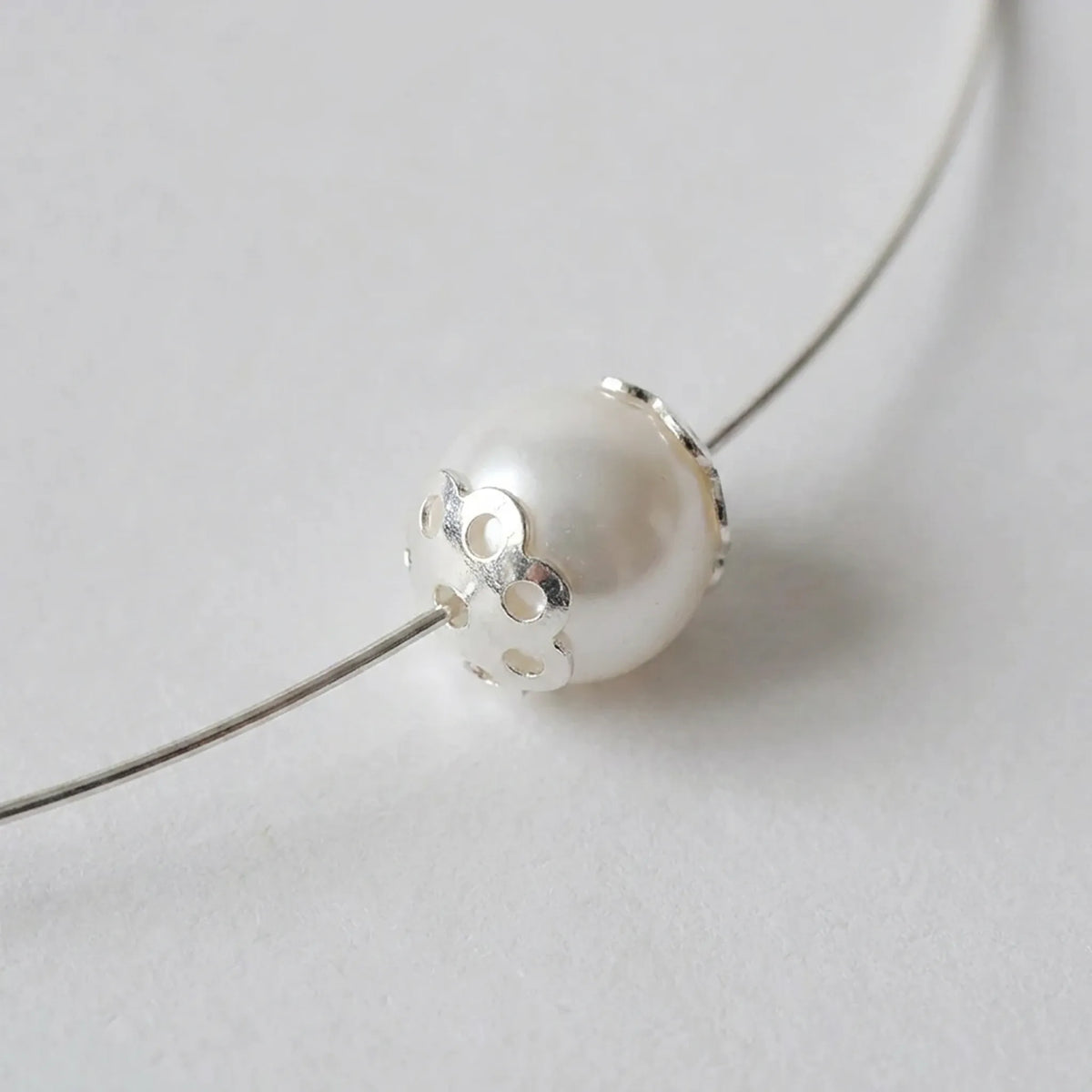 Sterling silver flower bead cap fitted against a pearl bead on jewelry wire