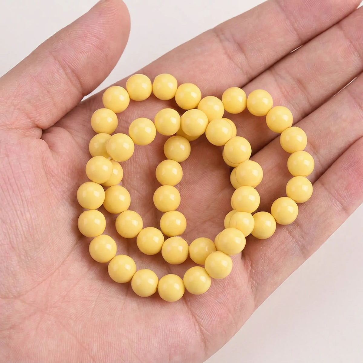 Yellow coated opaque glass round beads shown in hand for size comparison